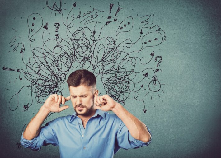 Ein Mann in einem blauen Hemd hält sich die Ohren zu, während verworrene Gedanken und Symbole über seinem Kopf schweben.