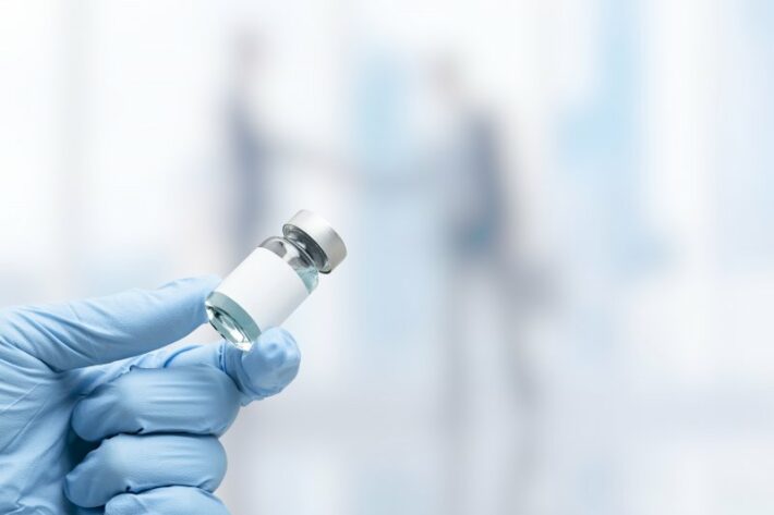 Eine Hand in blauen Handschuhen hält eine Glasvialspritze mit einer leeren Beschriftung.